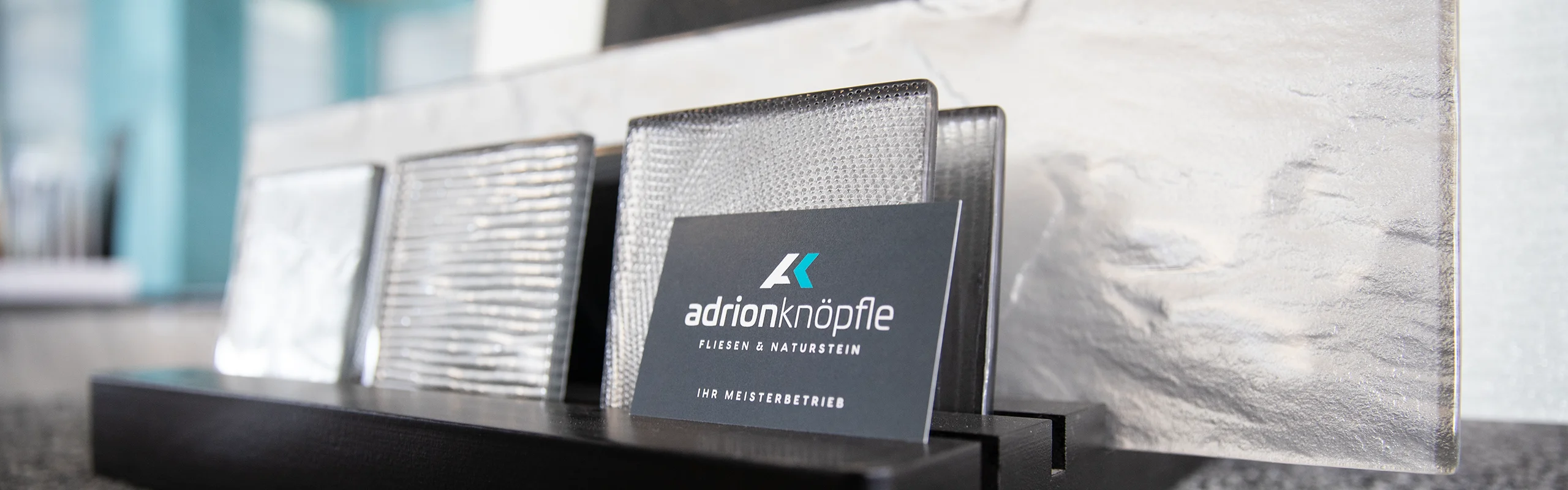 Visitenkarte der Firma Adrion Knöpfle vor Fliesenmuster